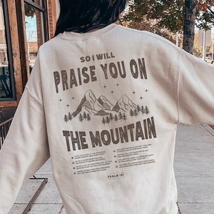May include: A beige sweatshirt with a graphic print of mountains and the text "So I will praise you on the mountain".