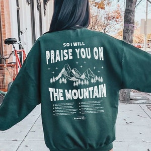 May include: Forest green sweatshirt with a white graphic of mountains and the text "So I will praise you on the mountain, Psalm 150:1".
