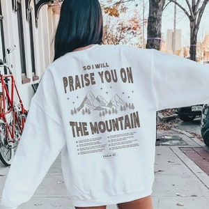 May include: White sweatshirt with a brown graphic print of mountains and the text "So I will praise you on the mountain".