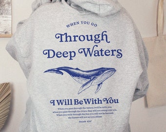 Puede incluir: Sudadera con capucha gris con un gráfico de ballena azul y el texto "When you go through deep waters I will be with you" y un versículo bíblico de Isaías 43:2.