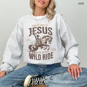 Puede incluir: Sudadera gris con un gr&aacute;fico marr&oacute;n de un vaquero montando un caballo. El gr&aacute;fico incluye el texto "PSALM XXIII:1-III JESUS RIDE ME ON THIS WILD RIDE".