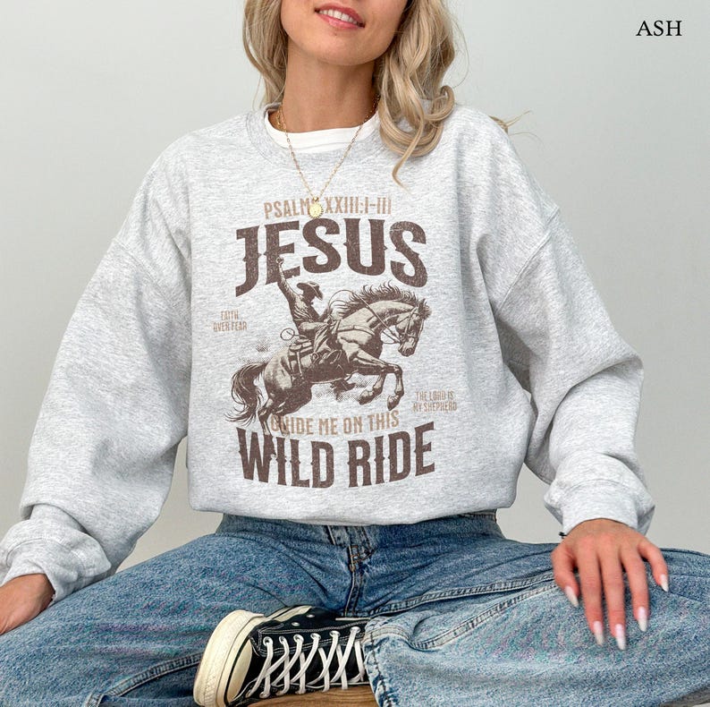 Puede incluir: Sudadera gris con un gr&aacute;fico marr&oacute;n de un vaquero montando un caballo. El gr&aacute;fico incluye el texto "PSALM XXIII:1-III JESUS RIDE ME ON THIS WILD RIDE".