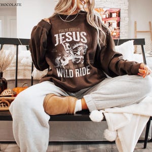 Puede incluir: Una sudadera marr&oacute;n con el texto "PSALMS XXIII:4-6 JESUS RIDE ME ON THIS WILD RIDE" y un gr&aacute;fico de una persona montando a caballo.