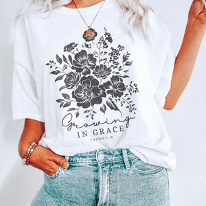 May include: White t-shirt with a black floral design and the text "Growing in Grace 2 Peter 3:18".