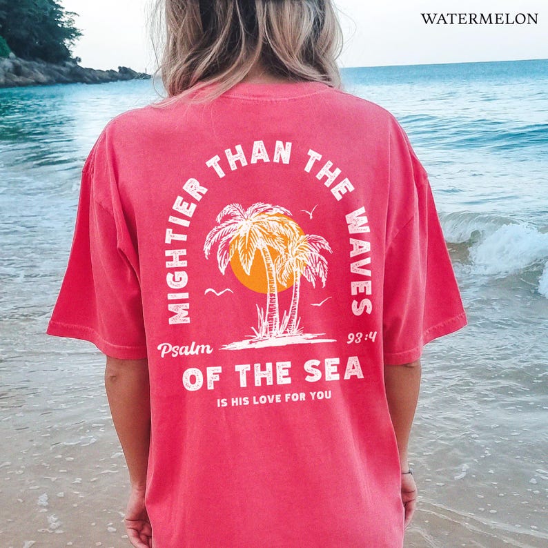 Puede incluir: Una camiseta roja con un dise&ntilde;o gr&aacute;fico blanco con palmeras y el texto "Mightier than the waves Psalm 93:4 of the sea is his love for you".