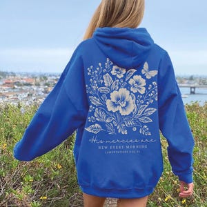 May include: A royal blue hoodie with a white floral design and the text "His mercies are new every morning - Lamentations 3:22-23" on the back.