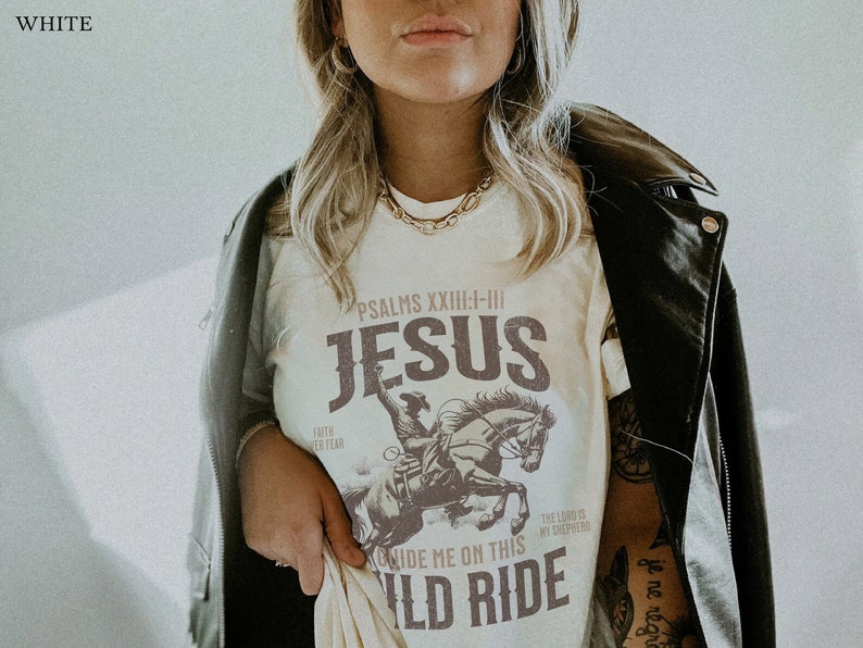 K&ouml;nnte beinhalten: Wei&szlig;es T-Shirt mit einer braunen Grafik eines Cowboys, der ein Pferd reitet. Der Text "PSALMS XXIII:I-III JESUS GUIDE ME ON THIS WILD RIDE" ist auf das T-Shirt gedruckt.