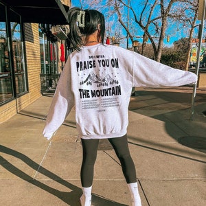 May include: A grey sweatshirt with a black graphic print on the back. The graphic features mountains and the text "So I will praise you on the mountain".