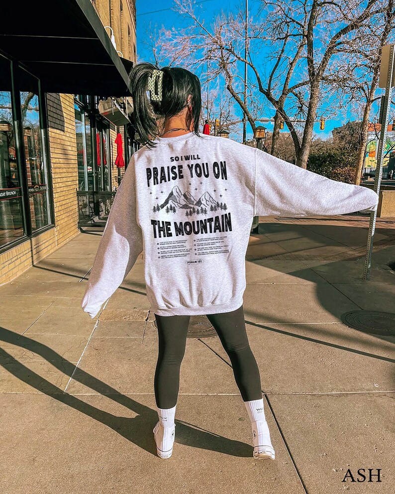 May include: A grey sweatshirt with a black graphic print on the back. The graphic features mountains and the text "So I will praise you on the mountain".