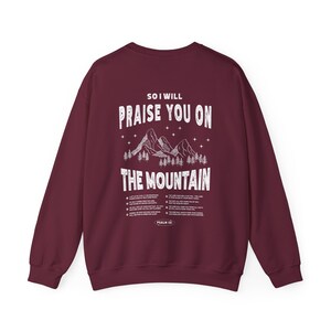 May include: Burgundy sweatshirt with a white graphic print of mountains and the text "So I will praise you on the mountain". The graphic also includes stars and trees. The text "Psalm 121" is printed at the bottom of the graphic.
