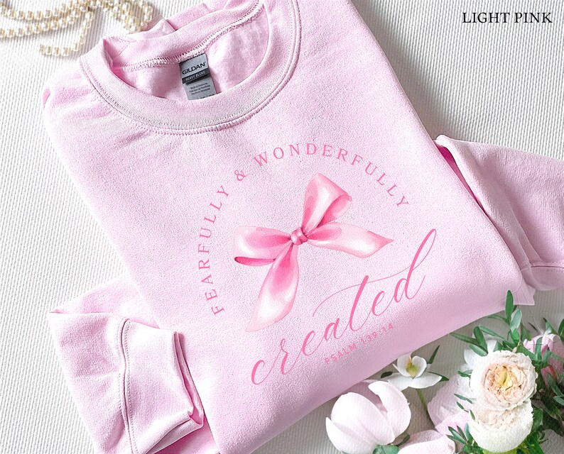 May include: Light pink sweatshirt with a pink bow and the text "Fearfully & Wonderfully Created" with the scripture reference "Psalm 139:14".