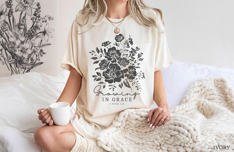 May include: A woman wearing a cream colored t-shirt with a black floral design and the text "Growing in Grace 2 Peter 3:18".