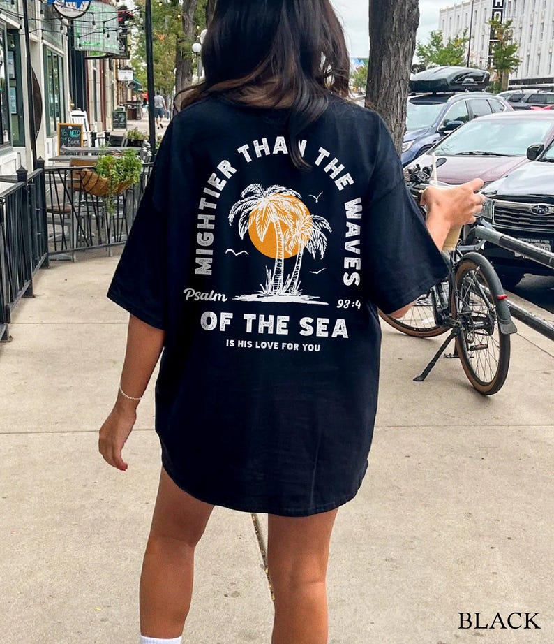 Puede incluir: Camiseta negra con un gr&aacute;fico blanco de palmeras y el texto "Mightier than the waves Psalm 93:4 Of the sea is his love for you".