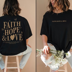 May include: Black oversized t-shirt with the text "FAITH HOPE & LOVE" in gold lettering on the front and back. The back also includes a small heart and butterflies. The shirt is being modeled by a person wearing light blue jeans.