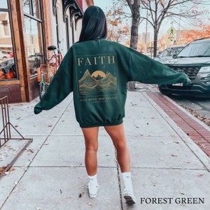 May include: Forest green sweatshirt with a gold graphic of mountains and a sun. The graphic includes the text "FAITH CAN MOVE MOUNTAINS MATTHEW 17:20".