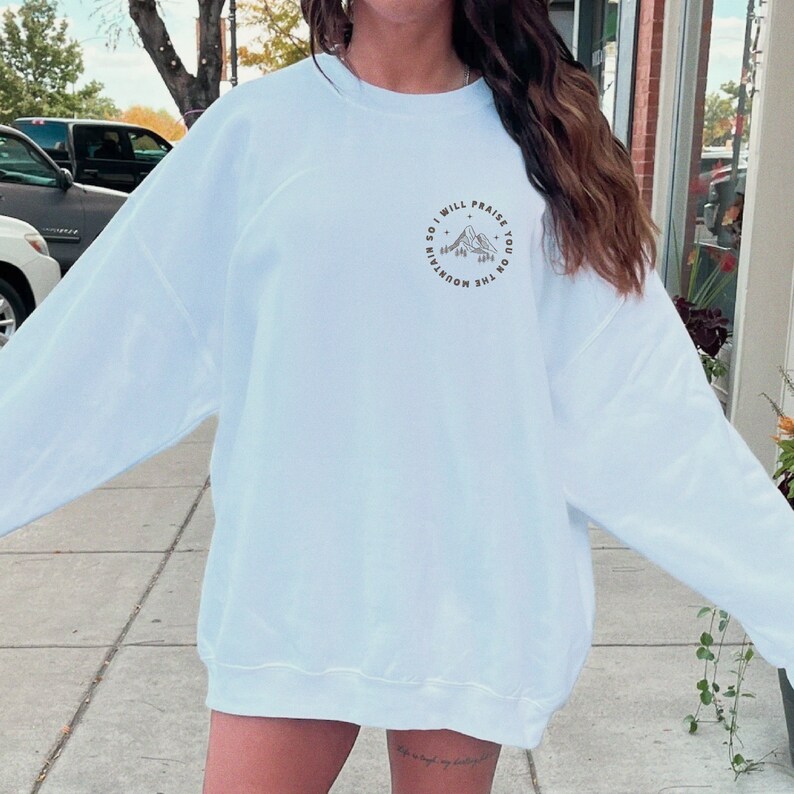 May include: A white sweatshirt with a graphic print of a mountain range and the text "So I will praise you on the mountain".