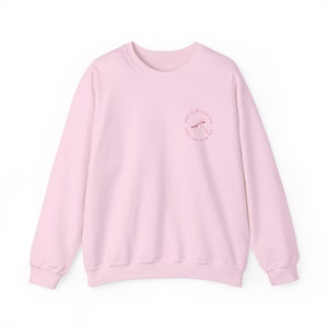 May include: A pink sweatshirt with a pink and white graphic design on the front. The graphic design features a dragonfly and the text "God is within me, I will not fall".