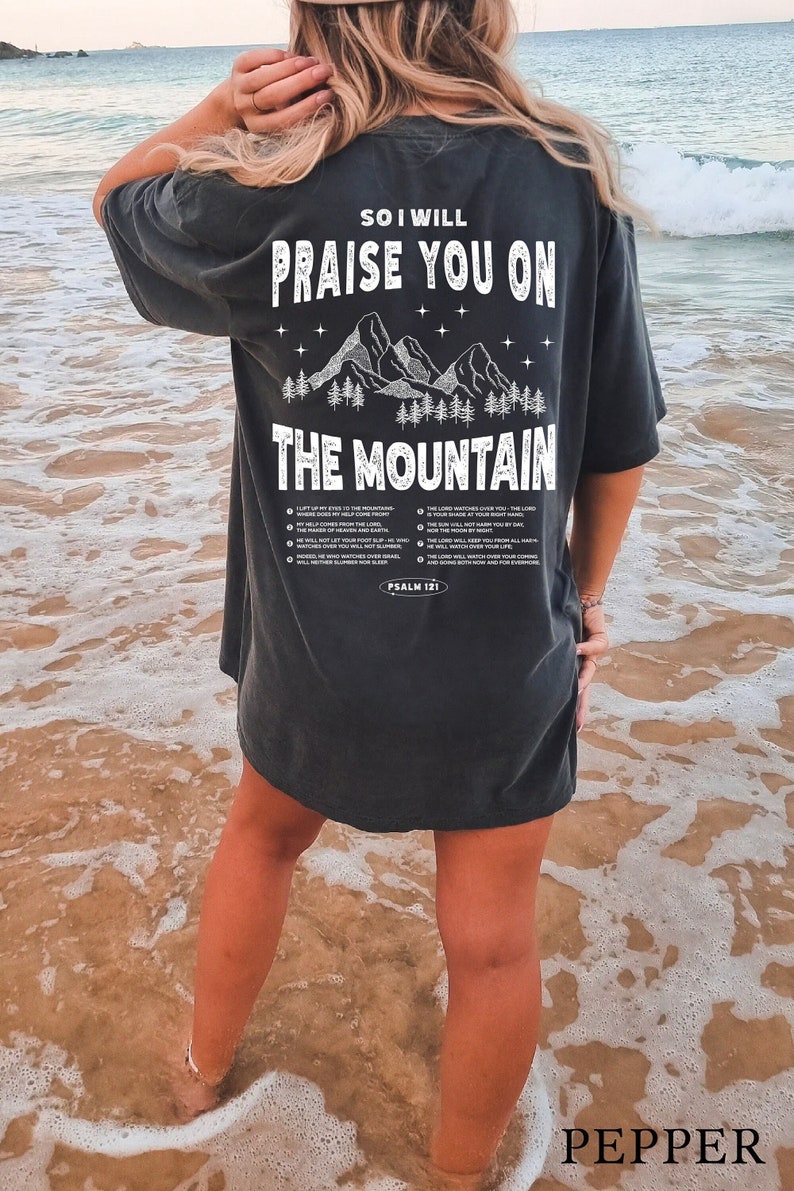 May include: Dark gray t-shirt with the text "SO I WILL PRAISE YOU ON THE MOUNTAIN" and a mountain graphic. The shirt also features text from Psalm 121. The word "PEPPER" is printed at the bottom.