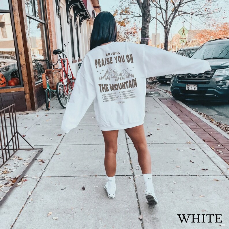 May include: White sweatshirt with a brown graphic print of mountains and the text "So I will praise you on the mountain".