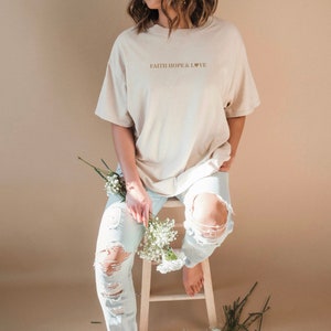 May include: A beige oversized t-shirt with the text "FAITH HOPE & LOVE" and a small heart symbol printed on the front.