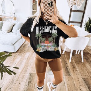 May include: Black t-shirt with a graphic print of a sunset with palm trees and the text "His Mercies". The graphic also includes the text "New For You" and "Lord Spring".