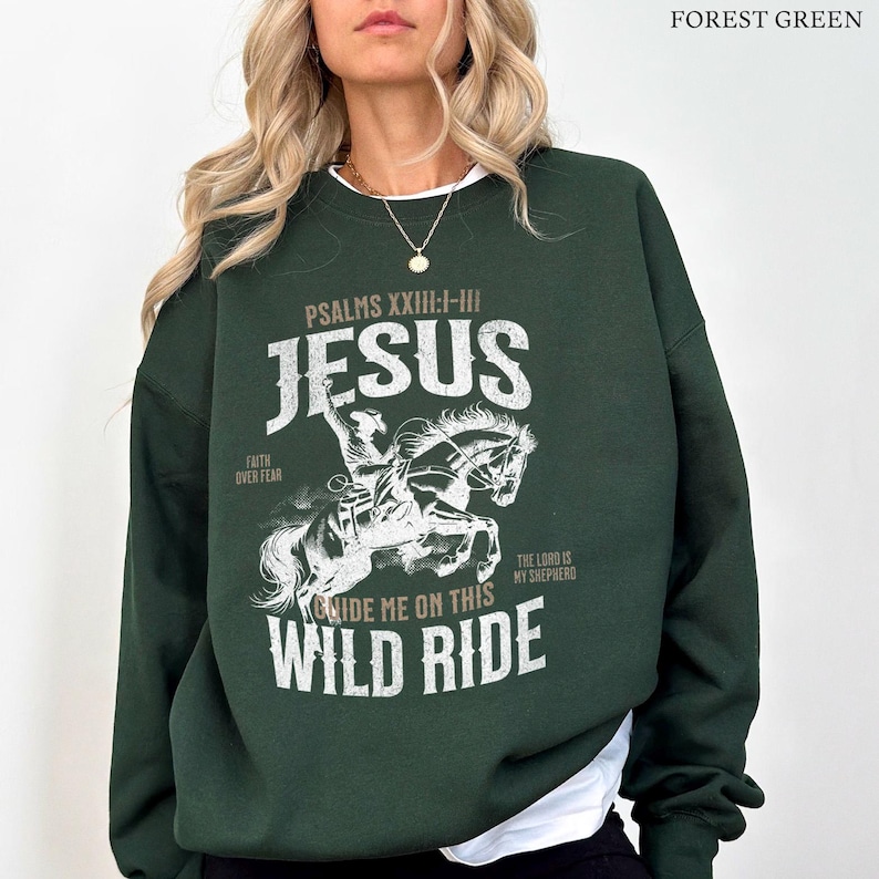 Puede incluir: Sudadera verde bosque con un estampado gr&aacute;fico blanco de una persona montando un caballo. El gr&aacute;fico incluye el texto "PSALMS XXIII:I-III JESUS", "FAITH OVER FEAR", "THE LORD IS MY SHEPHERD", y "RIDE ME ON THIS WILD RIDE".