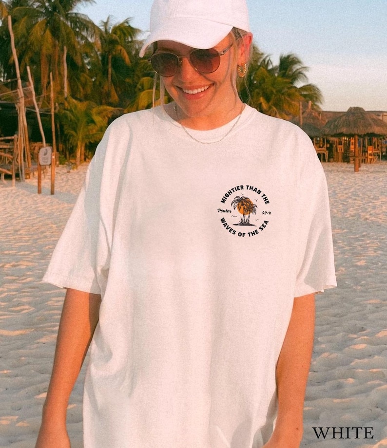Puede incluir: Camiseta blanca con un estampado gr&aacute;fico de una palmera y el texto "Mightier than the waves of the sea".