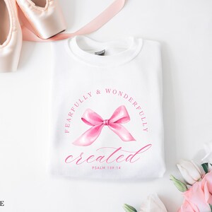 May include: White sweatshirt with a pink bow and the text "Fearfully & Wonderfully created Psalm 139:14" printed on the front.