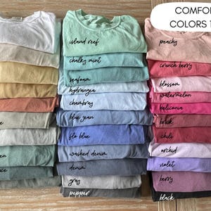 Puede incluir: Una colecci&oacute;n de 24 camisetas de varios colores, apiladas en filas. Los colores est&aacute;n etiquetados con nombres como "blanco", "marfil", "mantequilla", "mostaza", "yam", "piedra arenisca", "bah&iacute;a", "verde claro", "abeto azul", "musgo", "arrecife de isla", "menta cremosa", "espuma de mar", "hortensia", "chambray", "jean azul", "flo blue", "denim lavado", "denim", "gris", "pimienta", "melocot&oacute;n", "baya crujiente", "flor", "sand&iacute;a", "heliconia", "ladrillo", "chile", "orqu&iacute;dea", "violeta", "baya" y "negro".