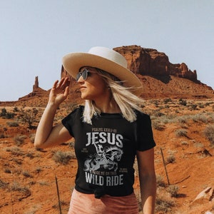 K&ouml;nnte beinhalten: Schwarzes T-Shirt mit einem wei&szlig;en Grafikdesign, das eine Person auf einem Pferd zeigt, mit dem Text "Psalms XXIII-4 Jesus Wild Ride" auf der Vorderseite.