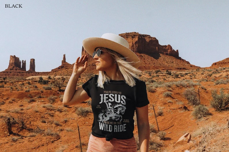 K&ouml;nnte beinhalten: Schwarzes T-Shirt mit einem wei&szlig;en Grafikdesign, das eine Person auf einem Pferd zeigt, mit dem Text "Psalms XXIII-4 Jesus Wild Ride" auf der Vorderseite.