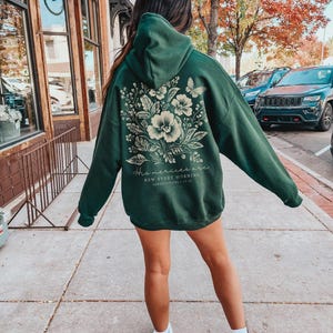 May include: Forest green hooded sweatshirt with a floral design and the text "His mercies are new every morning" in white. The sweatshirt is being worn by a person.