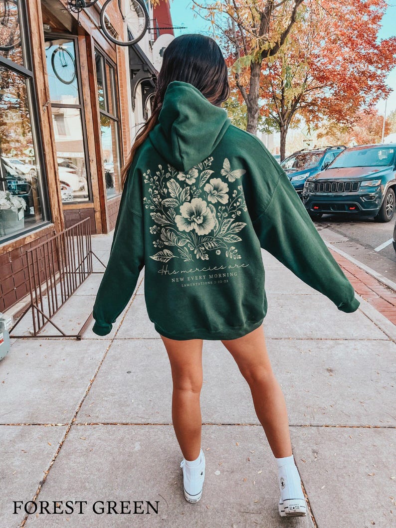 May include: Forest green hooded sweatshirt with a floral design and the text "His mercies are new every morning" in white. The sweatshirt is being worn by a person.