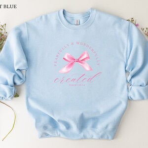 May include: Light blue sweatshirt with a pink bow and the text "Fearfully & Wonderfully Created" with the scripture reference "Psalm 139:14".