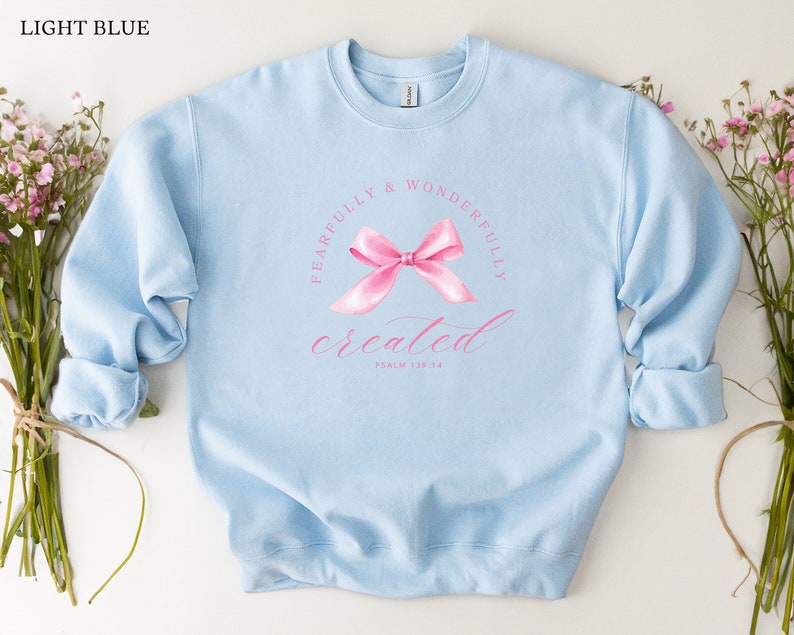 May include: Light blue sweatshirt with a pink bow and the text "Fearfully & Wonderfully Created" with the scripture reference "Psalm 139:14".