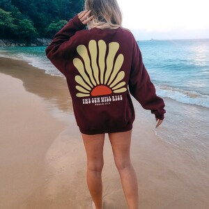 May include: A maroon sweatshirt with a yellow and orange sun graphic on the back. The text "THE SUN WILL RISE" and "PSALM 30:5" are printed below the graphic.