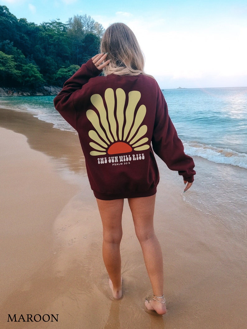 May include: A maroon sweatshirt with a yellow and orange sun graphic on the back. The text "THE SUN WILL RISE" and "PSALM 30:5" are printed below the graphic.