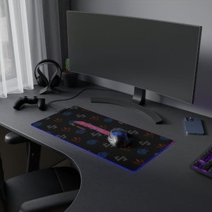 Könnte beinhalten: Schwarzes Gaming-Mauspad mit farbenfrohem Design und blau-rosa Rand. Das Pad hat ein Muster aus orangefarbenen, blauen und rosa Symbolen. Eine Gaming-Maus liegt auf dem Pad, neben einem Computermonitor und einer Tastatur.