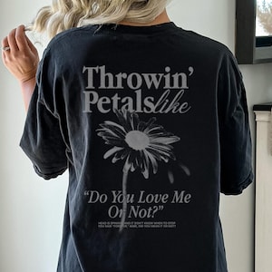 May include: Black t-shirt with the text "Throwin' Petals like" above a daisy graphic. Below the graphic, the text reads "Do You Love Me Or Not?" and a smaller line of text.