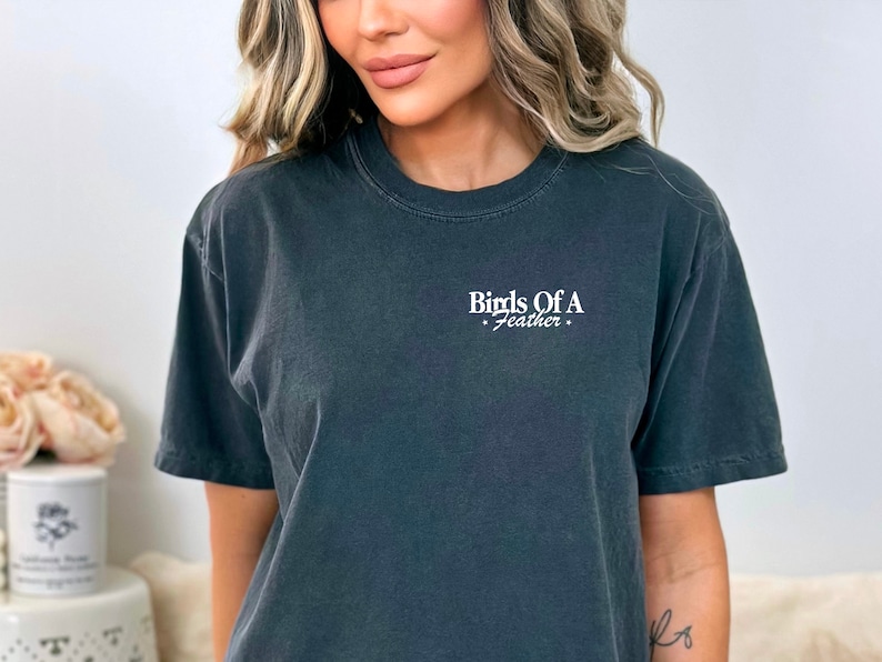 Peut inclure: Un t-shirt gris fonc&eacute; avec le texte "Birds Of A Feather" imprim&eacute; &agrave; l'avant en blanc.