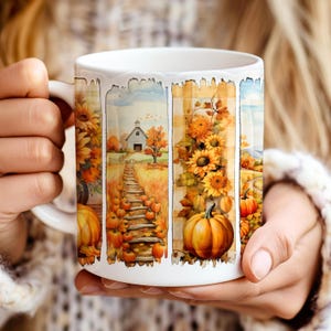 May include: White ceramic mug featuring a fall-themed design. The design includes sunflowers, pumpkins, a barn, and a wooden pathway. The mug is held by a person wearing a white sweater.
