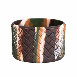 May include: A cylindrical silicone boot featuring a woven basket-weave texture. The material displays a marbled camouflage color pattern in shades of dark brown, forest green, tan, and white, with a smooth, solid rim at the top and bottom edges.