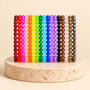 May include: A collection of eighteen vertical strands of faceted, multi-colored beads arranged in a spectrum sequence. The beads display a range of colors including red, pink, orange, yellow, green, blue, purple, black, brown, clear, and metallic gray.