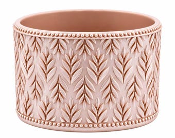 May include: A cylindrical blush pink planter featuring a repeating embossed leaf pattern across the exterior surface. The top and bottom edges are finished with a decorative beaded border, providing a textured detail to the vessel.
