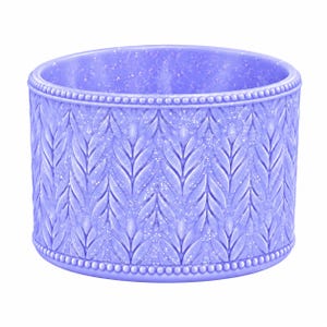 May include: A cylindrical lavender container featuring a raised leaf or wheat pattern across its exterior surface. The object has a beaded border along the top and bottom edges and is infused with fine glitter throughout the purple material.