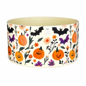 May include: A round ceramic bowl with a cream-colored background featuring a repeating pattern of orange jack-o'-lanterns, black and purple bats, a small white ghost, and various colorful flowers and green leaves scattered throughout.