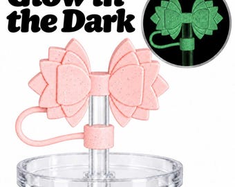 Puede incluir: Un adorno para pajita con forma de flor de loto rosa claro moteado con una fijación de bucle flexible, montado sobre un soporte circular transparente. El texto Glow in the Dark aparece arriba, con un recuadro circular que muestra el brillo verde.