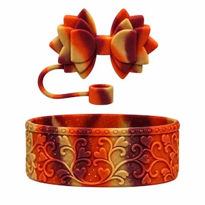 May include: A silicone bracelet and a matching bow-shaped charm with a tethered ring, both featuring a marbled blend of orange, red, and yellow colors. The bracelet has an embossed pattern of swirling vines and small hearts along its exterior.