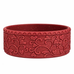 May include: A circular, deep red silicone bowl featuring a raised, embossed pattern of swirling vines and small hearts. The rim is decorated with a continuous border of tiny hearts, and the material has a subtle, fine gold-flecked texture.
