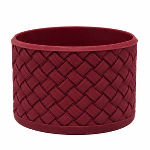 May include: A deep red, cylindrical container featuring a textured, woven basket-weave pattern across its exterior surface. The item has a smooth, solid rim at the top and a matching solid base, providing a uniform and structured appearance.